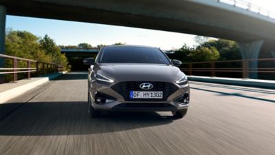 Front view of the new Hyundai i30 in grey, driving under a motorway bridge.