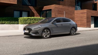 Vorderansicht des neuen Hyundai i30 Fastback in Grau, der vor einem modernen Haus geparkt ist.