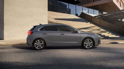 Vista lateral del nuevo Hyundai i30 en color gris aparcado en el exterior de una amplia escalera abierta.