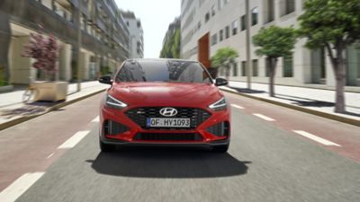 Vue avant de la nouvelle Hyundai i30 Fastback N Line en rouge, roulant dans une rue.