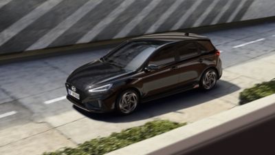 Ein Mann und eine Frau neben einem roten Hyundai i30 N Line, der vor einem modernen Wohnbungalow parkt.