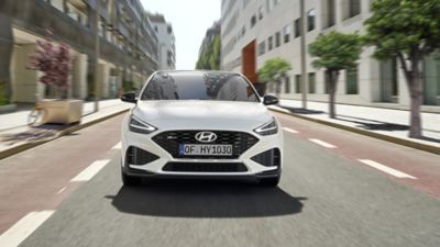 Ein Hyundai i30 Kombi N Line, von vorne gesehen, fährt auf einer baumbestandenen Innenstadtstraße.