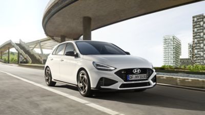 Ein Hyundai i30 Kombi N Line, schräg von vorne gesehen, fährt vor einer Hochhauskulisse unter einer Hochstraße hindurch.