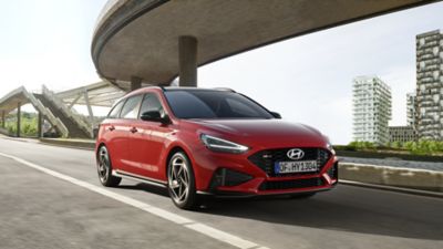 Three quarters view of the new Hyundai i30 Wagon N Line in red, parked under a bridge.