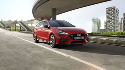 Vue de trois-quarts avant de la nouvelle Hyundai i30 Wagon N Line en rouge, garée sous un pont.