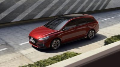 Žena stojící před Hyundai i30 N Line v červené zaparkované u domu.