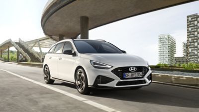 Ein Hyundai i30 Kombi N Line, schräg von vorne gesehen, fährt vor einer Hochhauskulisse unter einer Hochstraße hindurch.