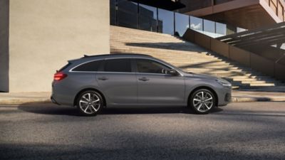 Vue latérale de la nouvelle Hyundai i30 Wagon en gris, garée devant un escalier large et ouvert.