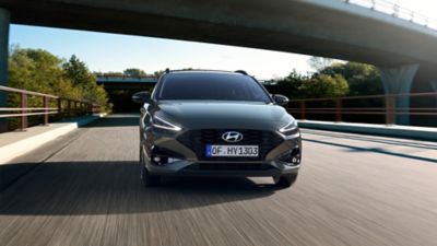 Front view of the new Hyundai i30 Wagon in grey, driving under a motorway bridge.