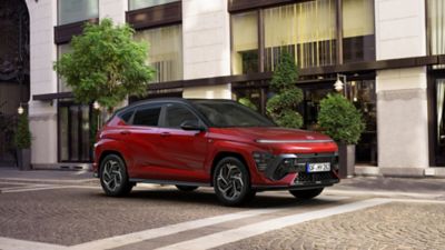 Le tout nouveau KONA Hybrid N Line rouge garé à côté d'un bâtiment moderne.