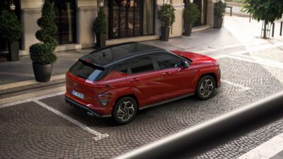 The all-new Hyundai KONA N Line in red parked in front of a building with several small trees. 