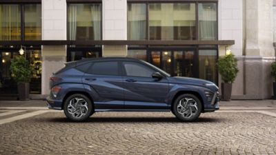 Nowy model Hyundai KONA stoi zaparkowany na ulicy, a kobieta pakuje bagaże do bagażnika.