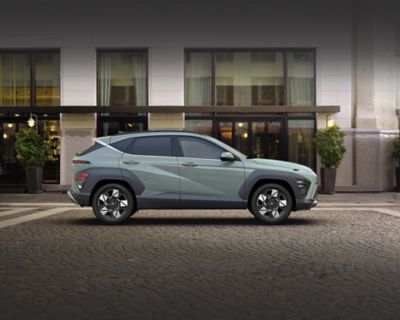 Zijaanzicht Hyundai KONA Mild-Hybrid, geparkeerd voor modern gebouw.