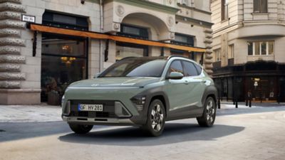 Driekwart vooraanzicht Hyundai KONA Mild-Hybrid geparkeerd in stedelijke omgeving met oude gebouwen.