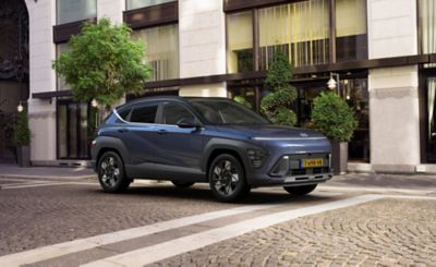 Een Hyundai KONA Hybrid geparkeerd op een klinkerweg in een moderne stadsomgeving.