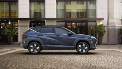 	Seitenansicht eines blauen Hyundai KONA, der vor einem städtischen Gebäude parkt.