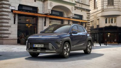 El nuevo Hyundai KONA en color verde circulando frente a un gran edificio de cristal.