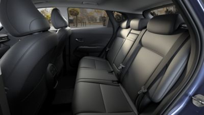 A woman sitting on the back seat of Hyundai KONA showing her smartphone to a friend outside. 