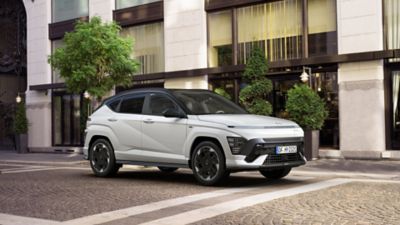 Zcela nový Hyundai KONA Electric N Line v bílé perleťové barvě Serenity zaparkovaný před hotelem.