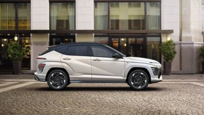 Zcela nový Hyundai KONA Electric N Line v bílé perleťové barvě Serenity zaparkovaný před hotelem.
