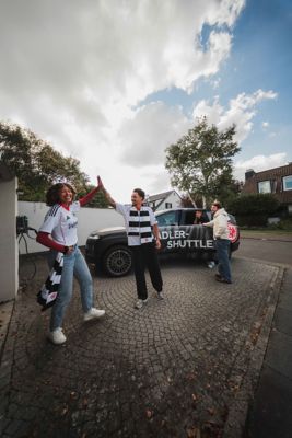 Eine Gruppe von Eintracht Frankfurt Fußballfans vor einem Hyundai IONIQ 6, der vor einer Hochhauskulisse parkt.