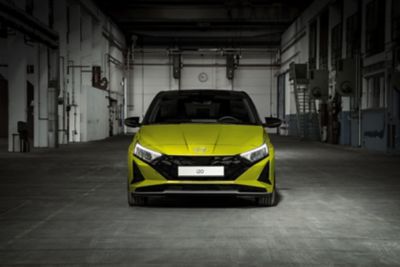 The new Hyundai i20 in profile in yellow parked in a chic industrial setting.