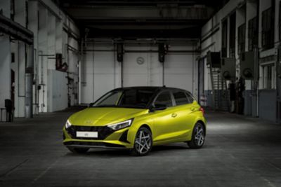 Nuova Hyundai i20 di profilo in giallo parcheggiata in un ambiente industriale chic.