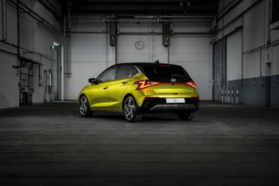 The new Hyundai i20 in profile in yellow parked in a chic industrial setting.