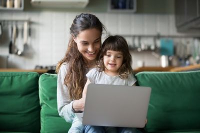Mother and daughter sitting on a green couch, laptop in front of them.