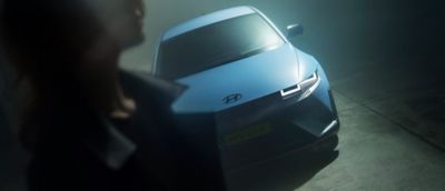 Vooraanzicht Hyundai IONIQ 5 N in diffuus donkere omgeving, met silhouet van persoon op voorgrond.