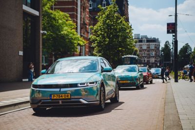Hyundai IONIQ 5 gehuld in kleuren van schilderij ‘Amandelbloesem’ van Vincent van Gogh in straat in Amsterdam.