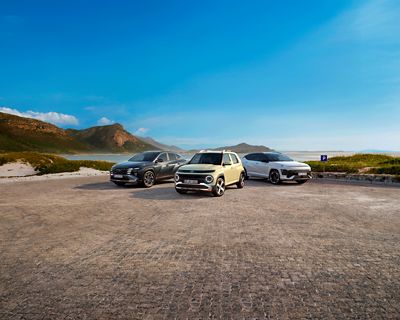 KONA Electric, KONA Hybrid et KONA Essence garés sur un parking devant des éoliennes