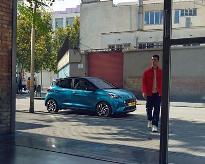 Hyundai i10 zijaanzicht blauw gekleurd met meneer in rode jas voor de auto