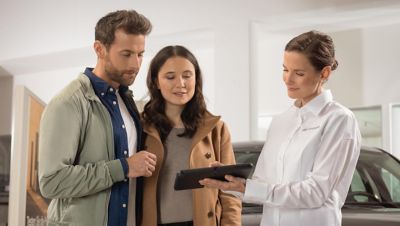 A Hyundai dealer with a tablet computer showing details about the Hyundai KONA to a couple. 	