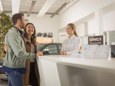 Un uomo e una donna sorridenti in piedi a un sportello informativo che parlano con un addetto della concessionaria Hyundai