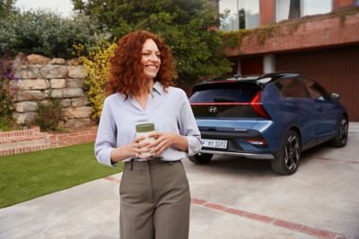 Vrouw staat op een oprit met op de achtergrond een geparkeerde Hyundai BAYON.
