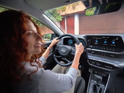 Vrouw in bestuurdersstoel heeft beide handen aan stuur Hyundai BAYON.