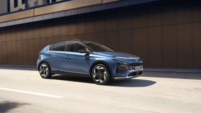 Side view of the new Hyundai BAYON in blue, with a concrete wall in the background.