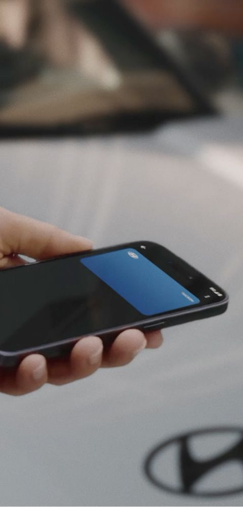 A close-up view of a hand holding a mobile phone with the background of the Hyundai BAYON N Line.