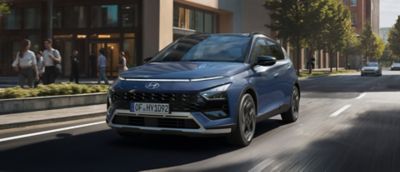 Ein Hyundai BAYON, schräg von der Seite gesehen, fährt in einer Stadt an Bäumen vorbei.