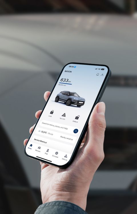 A close-up view of a hand holding a mobile phone with the background of the Hyundai BAYON N Line.