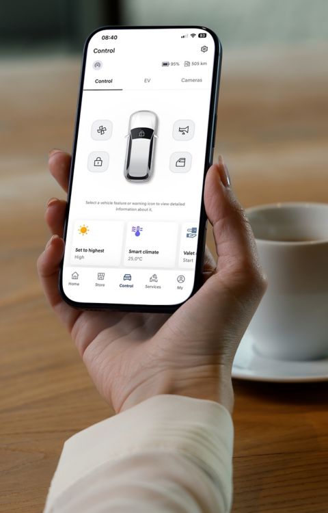 Hand holding a smartphone displaying an electric vehicle control app with remote climate settings and vehicle status.