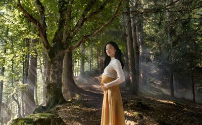 Photo d’une femme enceinte dans une forêt mettant ses mains sur son ventre.