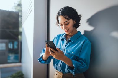 A woman leaning against a wall and looking at her mobile phone.