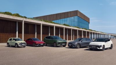 Five Hyundai EV cars parked side by side in front of a modern building, under a clear blue sky.