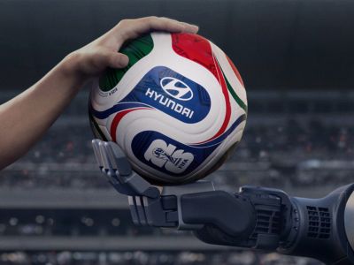 A human hand and a robot hand holding a football together with Hyundai logo on it.