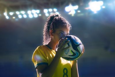 A female footballer in a yellow jersey kissing a football.