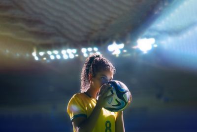 Een vrouwelijke voetballer in een gele trui kust een voetbal.