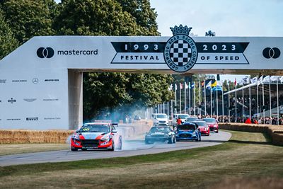 Racing cars driving under the Goodwood Festival of Speed archway.