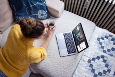 En dame med kaffekopp ser på en laptop. Foto.